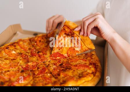 Vue rapprochée de la jeune femme adulte méconnue qui prend une part de pizza italienne savoureuse et chaude de la boîte ouverte, service de livraison de nourriture. Banque D'Images