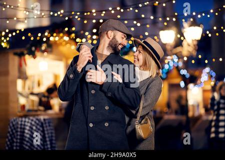 Les amoureux de Noël romance dans la rue le soir de Noël.Un jeune couple heureux dans l'amour souriant et embrassant tout en regardant les uns les autres et debout sur Banque D'Images