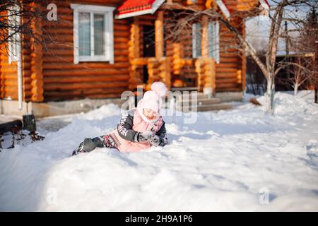 L'enfant joue dans la nature.Petite fille sur fond de promenades de chalet en bois dans l'arrière-cour, fait bonhomme de neige et joue des boules de neige le jour ensoleillé d'hiver Banque D'Images