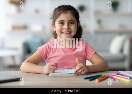 Jolie petite fille arabe assise au bureau à la maison, dessin dans le Bloc-notes Banque D'Images