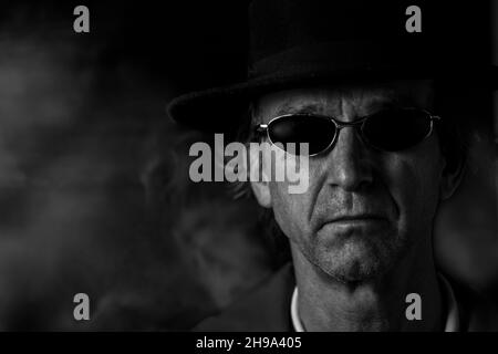 Photo de tête noire et blanche d'un homme caucasien avec lunettes de soleil et chapeau Banque D'Images