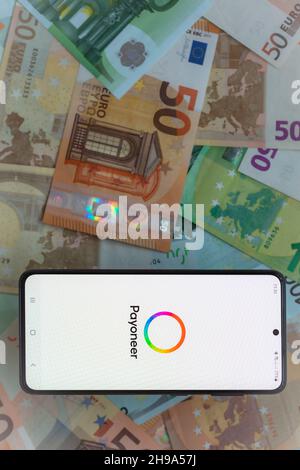 New York, Etats-Unis- 1 décembre 2021: Écran smartphone avec service de paiement numérique application mobile Payoneer sur fond de billets en euros Banque D'Images