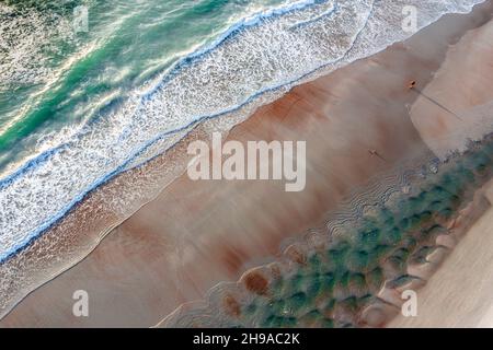 Vue aérienne de la plage de Floride avec une femme marchant sur du sable humide entre les bassins de marée d'aqua et l'océan Atlantique entrant. Banque D'Images