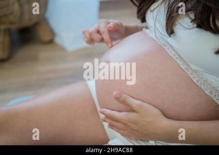 Une femme enceinte méconnue se reposant sur le sol et touchant doucement le ventre Banque D'Images