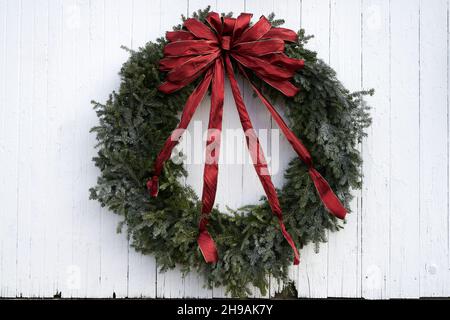Couronne de vacances naturelle à feuilles persistantes avec rubans rouges sur parement en bois rustique ancien avec peinture écaillée Banque D'Images