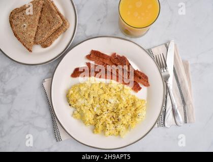 Vue sur une assiette de bacon et d'œufs brouillés avec pain grillé au grain entier et un verre de jus d'orange frais Banque D'Images