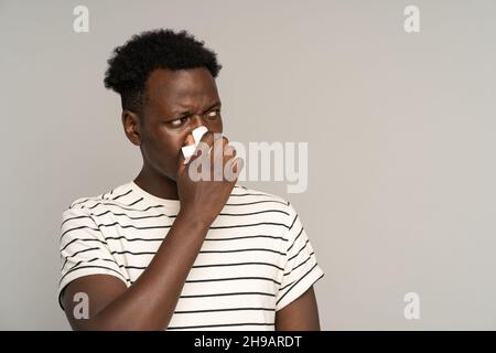 Homme africain malade souffrant de symptômes d'allergies saisonnières, malade mec noir soufflant le nez dans les tissus Banque D'Images