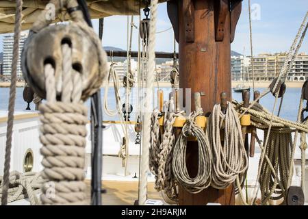 Cordes enroulées autour du mât d'un ancien voilier dans le port de Palamós avec des bâtiments en arrière-plan. Banque D'Images