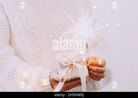 Une fille dans un chandail blanc tient un cadeau et des Sparklers étincelants.Concept de vacances nouvel an ou Noël.Mise au point sélective Banque D'Images