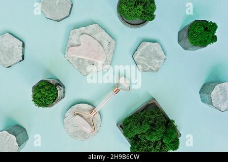 Gua Sha masseur et rouleau de quartz rose sur des podiums en béton sur fond bleu.Pose à plat. Banque D'Images