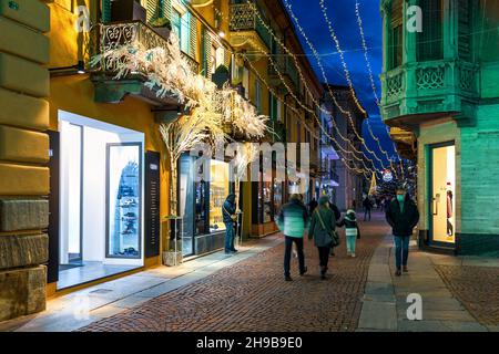 Personnes marchant dans une rue pavée illuminée de lumières de Noël dans la soirée dans le centre historique d'Alba, Italie. Banque D'Images