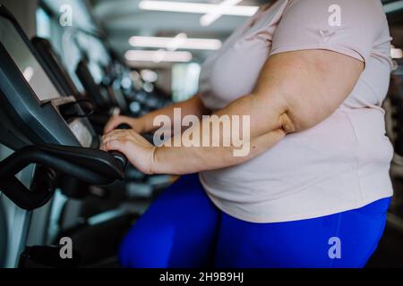 Milieu de section de femme en surpoids s'exerçant sur un tapis roulant à l'intérieur dans la salle de gym Banque D'Images