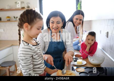 Petites filles heureuses avec la mère et la grand-mère faire des crêpes à l'intérieur à la maison, la cuisine. Banque D'Images