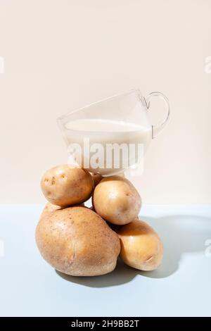 Lait de remplacement.Composition moderne avec une tasse de lait de pomme de terre qui équilibre sur un tas de pommes de terre. Banque D'Images