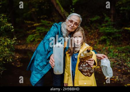 Petite fille avec grand-mère montrant les déchets de plastique ce qu'ils ont trouvé des outoors en forêt. Banque D'Images