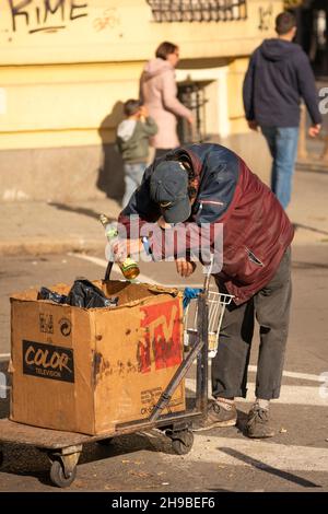 Homme sans abri tenant une bouteille à la main poussant un chariot dans les rues.Concept de désespoir.Sofia, Bulgarie, Europe de l'est, UE Banque D'Images