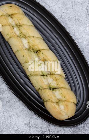 Baguette à pain à l'ail et aux herbes sur une assiette en granit noir.Sur un fond concret Banque D'Images