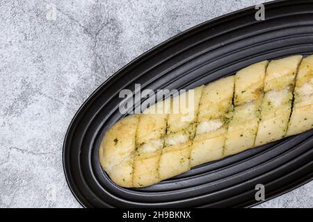 Baguette à pain à l'ail et aux herbes sur une assiette en granit noir.Sur un fond concret Banque D'Images