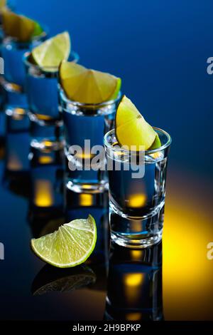 Tequila avec des tranches de citron vert sur un fond réfléchissant noir. Banque D'Images