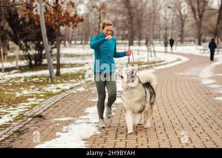 Femme jouant avec son chien tout en marchant dans le parc le jour d'hiver enneigé.Animaux de compagnie, neige, amitié, activités du week-end Banque D'Images