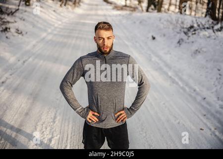Tenir le sportif debout sur un sentier enneigé dans la nature et tenir les mains sur les hanches.Sport d'hiver, gagnant, réalisation Banque D'Images