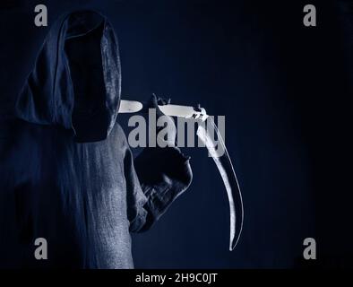 Mort tenant un vieux scythe lame aiguisée sur les épaules de la mort dans l'obscurité bleue peur et terreur Banque D'Images