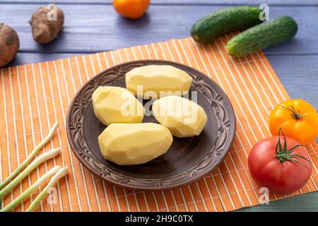 Des tubercules de pommes de terre épluchés crus sur une assiette de la table de cuisine avec des légumes.Préparation de la cuisson. Banque D'Images