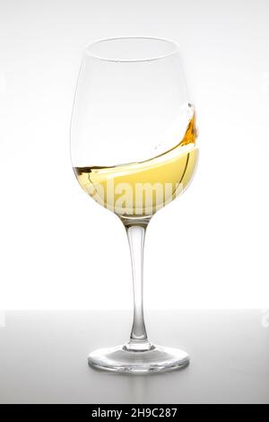 Vin blanc tourbillonnant en verre sur fond blanc Banque D'Images