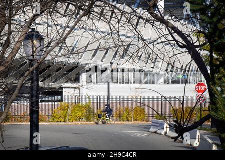 Un homme sur un vélo pliant passe par le stade Louis Armstrong tel que photographié à travers les arbres dans le parc de Flushing Meadows Corona à Queens, New York. Banque D'Images