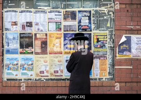 Un juif hassidique avec un long peyot maurique lit principalement des annonces et des publicités yiddish sur un mur de la communauté à Williamsburg, Brooklyn, New York. Banque D'Images