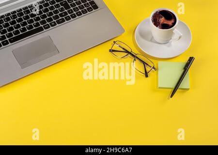 Studio photo avec un arrière-plan jaune d'un ordinateur portable à côté d'une tasse de café, de verres et de papeterie Banque D'Images