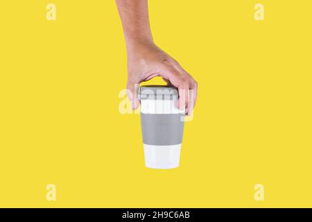 Photo de studio avec fond jaune d'une main tenant une tasse de café en plastique à emporter Banque D'Images