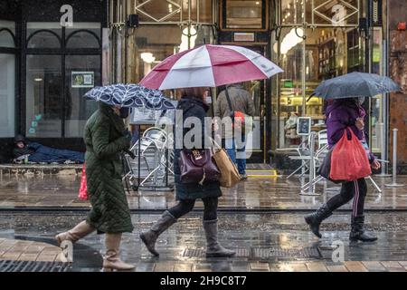 Magasins, amateurs de shopping avec parasols sur une plage humide et venteuse à Preston, Lancashire.Shopping dans le centre-ville par une journée humide et venteuse.Un avertissement météo pour les vents de 50mph est prévu pour entrer en vigueur à l'approche de Storm Barra.Crédit : MediaWorldImages/AlamyLiveNews Banque D'Images