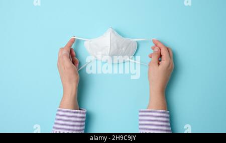 la main femelle tient un masque médical blanc jetable contre les maladies virales, fond bleu, vue de dessus Banque D'Images