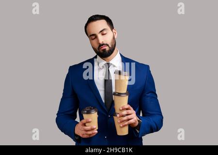 Des tasses de café d'homme d'affaires fatiguées et dormante, se sentant épuisé s'ennuyer après une journée de travail stressante, portant un costume de style officiel.Prise de vue en studio isolée sur fond gris. Banque D'Images