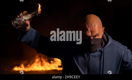 Un homme masqué tient une bouteille brûlante. Cocktail Molotov. Banque D'Images