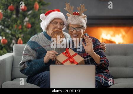 Un couple senior discute avec quelqu'un en utilisant un ordinateur portable dans la salle de séjour décorée pour Noël. Banque D'Images