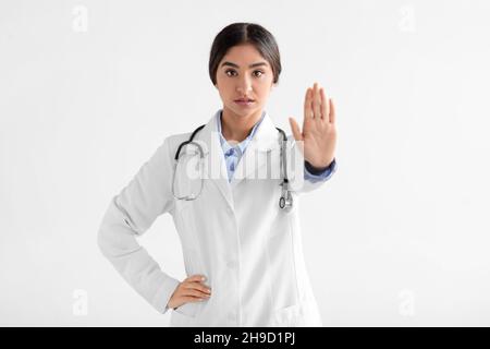 Femme hindoue sérieuse millénaire médecin en manteau montrant un geste de la main d'arrêt, isolée sur fond blanc Banque D'Images