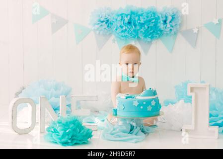 Fête d'anniversaire pour un garçon d'un an dans des guirlandes bleues et turquoise et un gâteau, concept de vacances et décor, un enfant avec un gâteau Banque D'Images