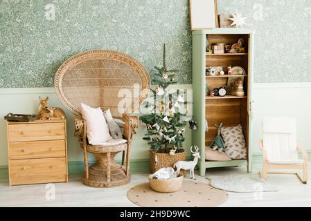 La décoration de la chambre des enfants du nouvel an : un fauteuil en osier avec oreillers, un sapin de Noël avec jouets, une armoire et une commode en styl vintage Banque D'Images