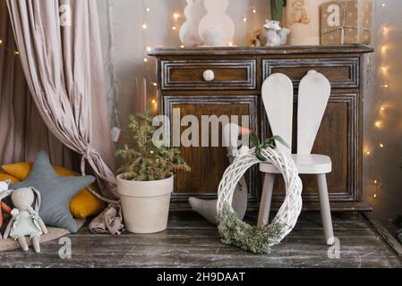 Décoration de Noël et du nouvel an de la chambre des enfants pour les vacances : un arbre dans un pot, une chaise sous forme de lapin, des lumières, des oreillers et des jouets Banque D'Images