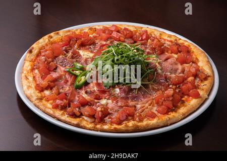 pizza au jambon avec tomates, fromage et nappée de piments verts et d'arugula Banque D'Images