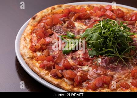 pizza au jambon avec tomates, fromage et nappée de piments verts et d'arugula Banque D'Images