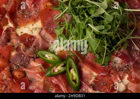 pizza au jambon avec tomates, fromage et nappée de piments verts et d'arugula Banque D'Images