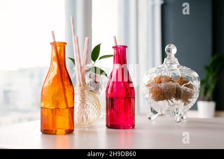 Bouteilles en verre colorées avec pailles en papier pour boissons ou cocktails et un bol de biscuits Banque D'Images