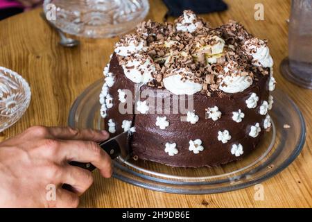 Gâteau au chocolat avec crème fouettée et bananes en cours de coupe Banque D'Images