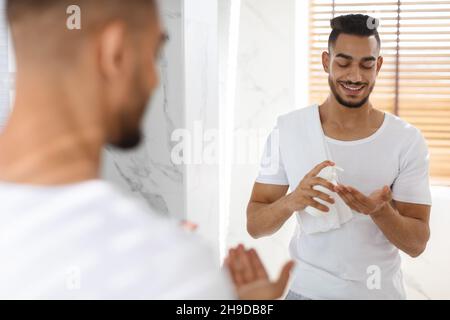 Soins de la peau pour hommes.Beau jeune homme arabe utilisant la lotion après-rasage dans la salle de bains Banque D'Images