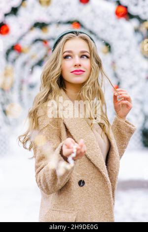 Une jolie jeune femme tient dans sa main les lumières d'une guirlande sur le fond d'un marché de Noël Banque D'Images