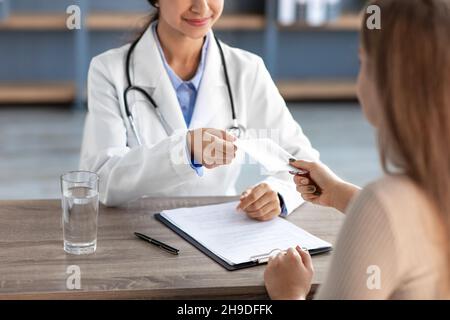 Pantacourt sourire millénaires indienne médecin en manteau blanc prendre l'argent du client dans le bureau de la clinique Banque D'Images