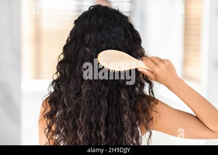 Vue arrière de la jeune femme Brunette peignant les cheveux bouclés avec la brosse Bamboo Banque D'Images